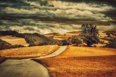 Road passing through field against cloudy sky