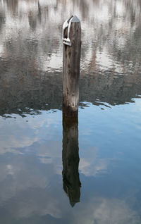 Wooden post in lake against sky