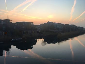 Reflection of buildings in river against sky during sunset