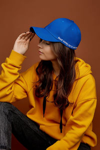 Young woman looking away while sitting against yellow wall