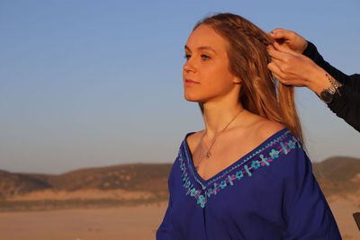 Portrait of young woman looking away against clear blue sky