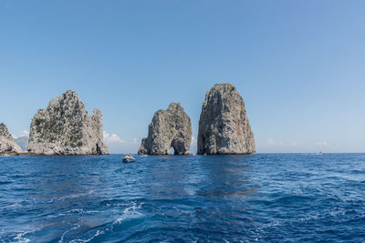 Rock formation in sea against clear blue sky