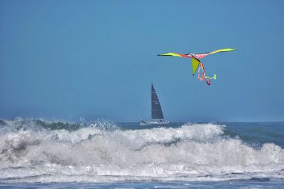 Kite flying over sea against clear blue sky