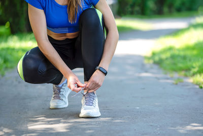 Low section of woman tying shoelace while crouching on road
