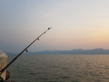 Fishing rod over sea against sky during sunset