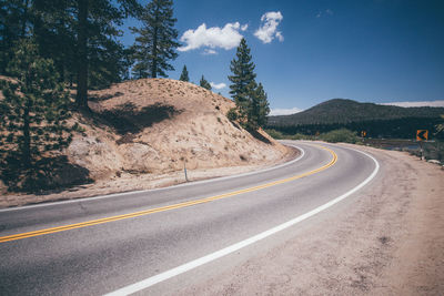 View of country road by trees against sky