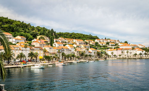 Boats moored at harbor by houses against sky