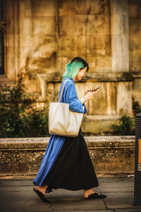 Side view of woman using mobile phone while walking on street