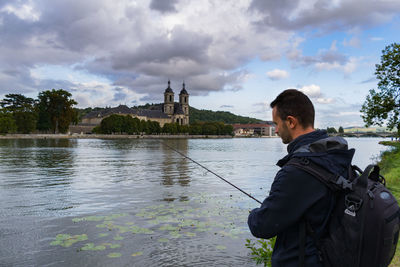 Rear view of man standing by river against sky