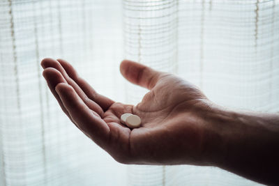 Close-up of human hand holding medicines by curtain at home