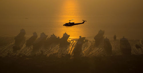 Silhouette airplane flying over beach against sky during sunset