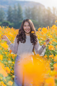 Portrait of woman standing by yellow flowering plants