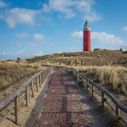 Road leading towards lighthouse amidst buildings against sky