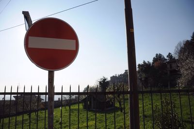 Road sign by fence against clear sky
