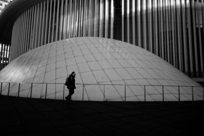 Man walking on footpath against modern building in city