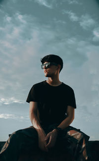 Young man looking away while sitting against sky