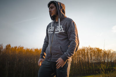 Young man looking away on field against sky