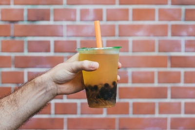 Close-up of hand holding drink against brick wall