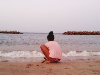Rear view of girl sitting on beach against clear sky