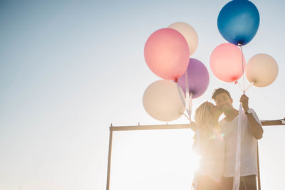 Couple standing with balloons against sky