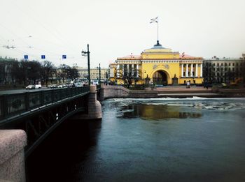 Bridge over river by buildings against sky in city