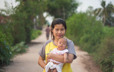 Portrait of woman carrying toddler son while standing on footpath