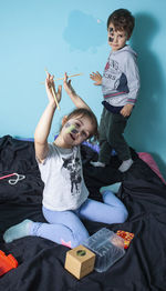 Full length of siblings sitting on bed