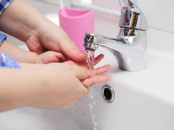 Close-up of person and baby washing hands in bathroom sink