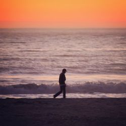 Man walking at beach against sky during sunset