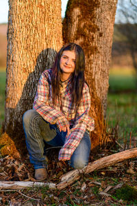 Portrait of young woman sitting by oak trees 