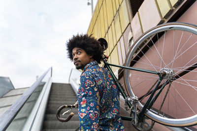 Stylish man carrying bicycle on escalator