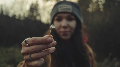 Close-up of woman showing white flower while standing outdoors