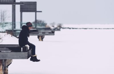 Side view of woman sitting on pier against sky during winter