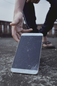 Low section of man holding broken smart phone on road
