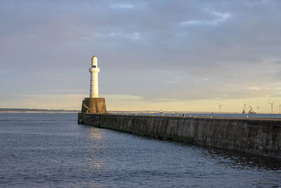 Lighthouse by sea against sky during sunset