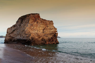 Rock formation on sea shore against sky