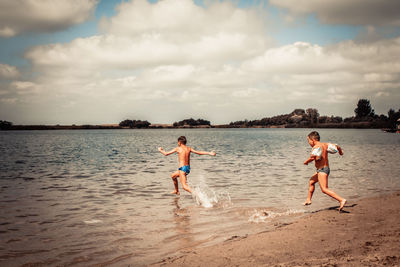 Children running at beach against sky