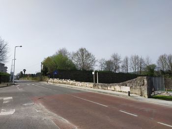 Empty road by trees against clear sky