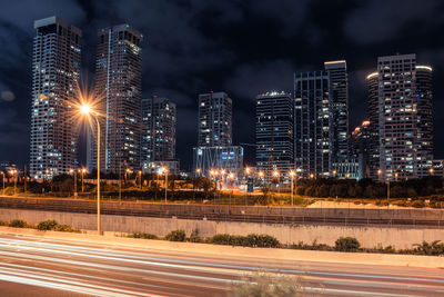 Illuminated city by buildings against sky at night