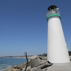 Lighthouse by sea against clear sky