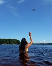Woman reaching airplane while standing in sea against blue sky