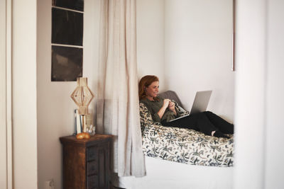 Smiling woman using laptop on bed