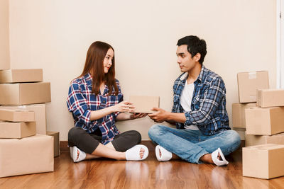 Couple holding cardboard boxes while sitting on floor at new home