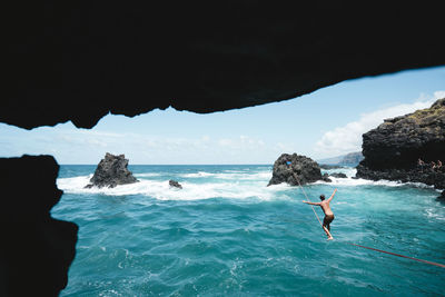 Full length of shirtless young man practicing slacklining over sea