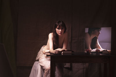 Portrait of shirtless young woman sitting on table with mirror