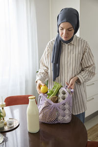 Woman in headscarf unpacking groceries at home