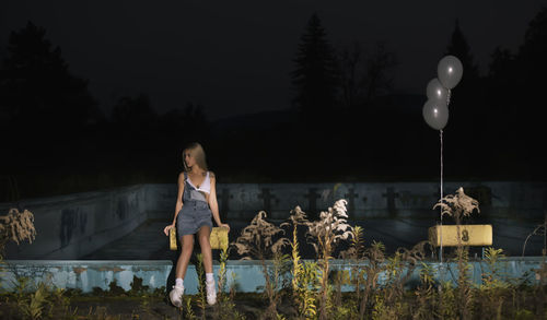 Young woman sitting on diving platform at swimming pool during night