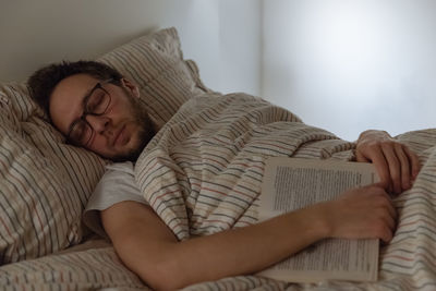 Adult man fell asleep with a book in hands in bed. accumulated fatigue, not enough sleep