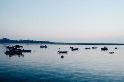 Boats in calm sea against clear sky