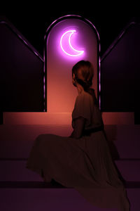 Woman from behind with a moon-shaped neon light